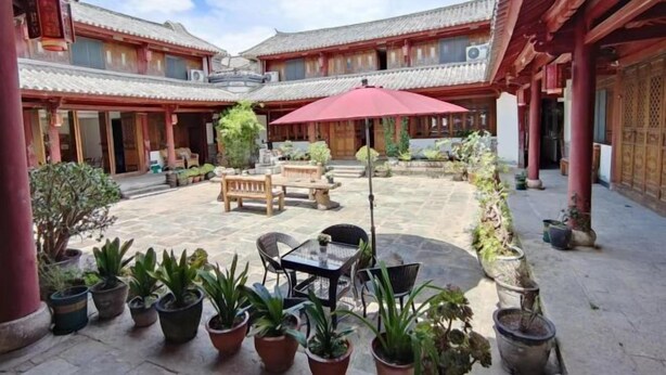 A courtyard with traditional architecture, featuring potted plants, a wooden table, and a red umbrella. - Yahve Academy Hotel (Dali City)