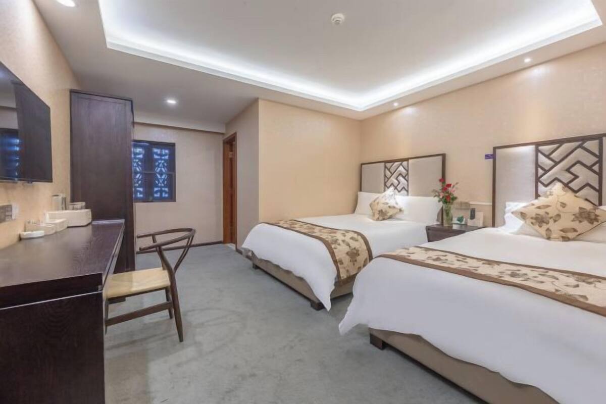 A hotel room with two beds, a desk, a chair, and a large window with a view.