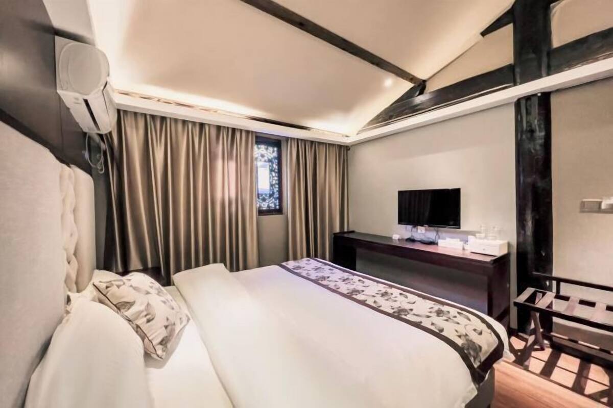 A hotel room with a bed, a desk, a chair, a television, and a window with curtains.