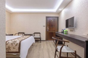 Una habitación de hotel con una cama, dos sillas, un escritorio, un televisor y una puerta.