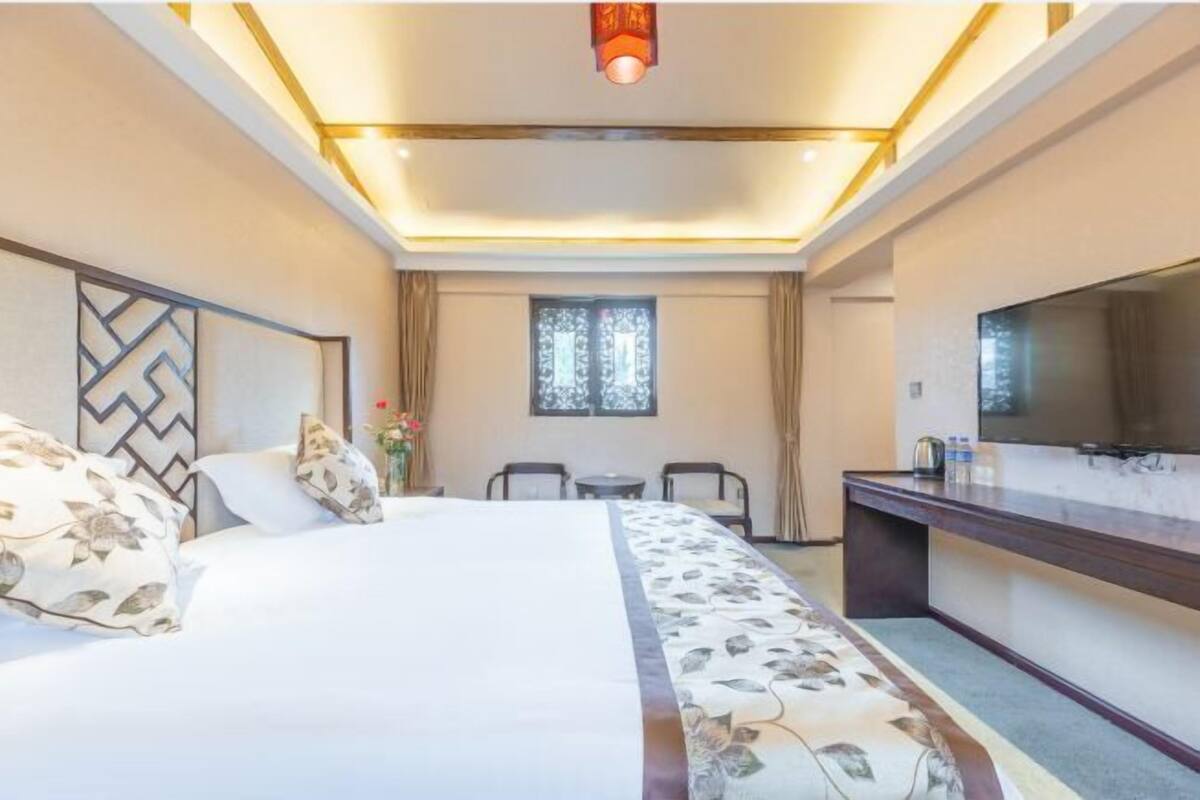 A hotel room with a large bed, a desk, a chair, and a window with curtains.