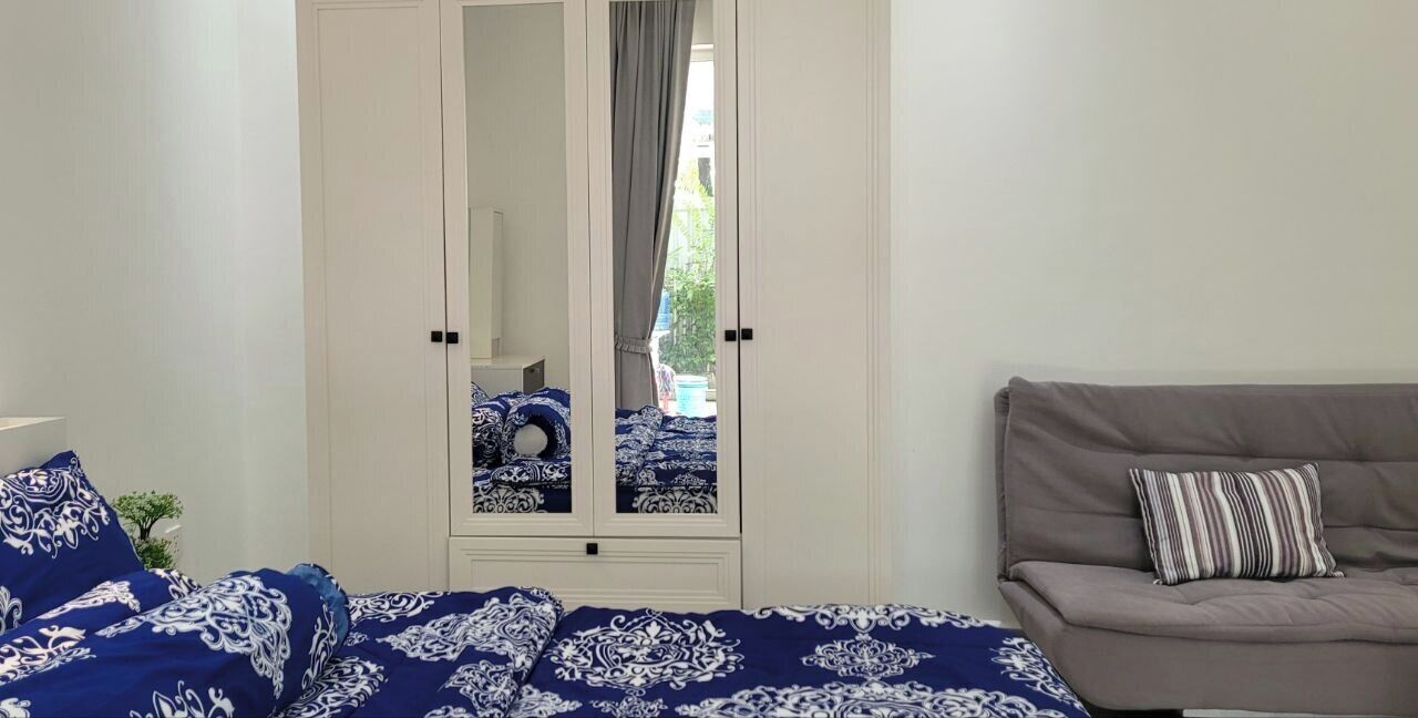 Une chambre avec un lit, un canapé gris, un miroir et une vue sur l’extérieur.