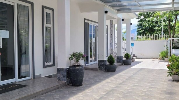 A covered outdoor area with potted plants, a doormat, and a pathway leading to a building with glass doors. - The Pepperian Homestay (Kampot)