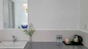 A bathroom with a white sink, a mirror, a small plant, and toiletries on the counter. - The Pepperian Homestay (Kampot)
