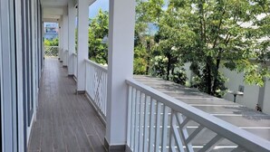 A covered corridor with a wooden floor, white railings, and a view of trees and buildings in the background. - The Pepperian Homestay (Kampot)