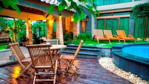 A wooden deck with outdoor furniture, a swimming pool, and lush greenery. - Maharani Guest House (Yogyakarta)