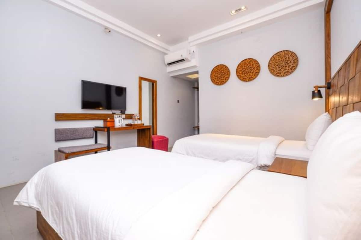 Una habitación de hotel con dos camas, televisor, escritorio y espejo.
