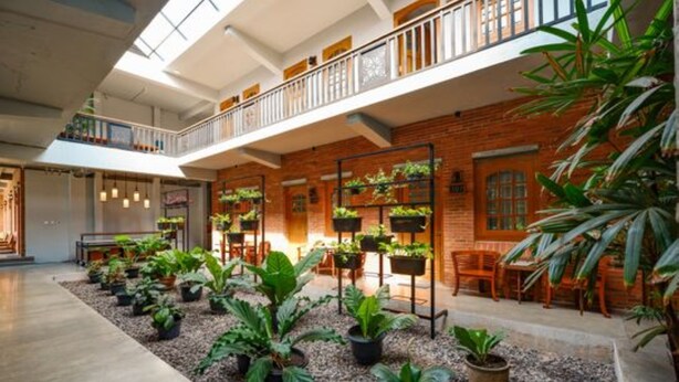 A spacious indoor area with a mezzanine level, brick walls, and multiple seating areas with potted plants. - Maharani Guest House (Yogyakarta)