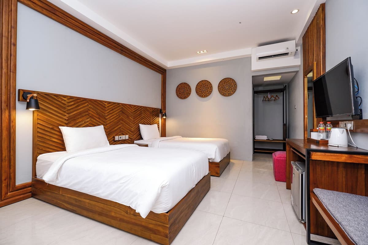 Habitación de hotel con dos camas, televisor, escritorio y armario.