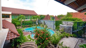 A courtyard with a swimming pool, surrounded by greenery and buildings with red-tiled roofs. - Maharani Guest House (Yogyakarta)