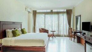 A hotel room with a large bed, a desk with a computer, a chair, and a TV. - Maharani Guest House (Yogyakarta)