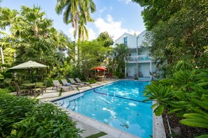 A swimming pool surrounded by lush greenery, a covered seating area, and a two-story building with balconies. - Coco`s Poolside Retreat (Key West)