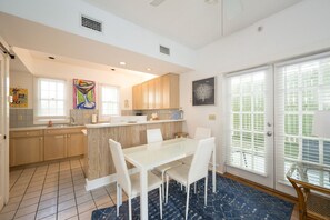A modern kitchen with white cabinets, a central island, and a dining area with a glass table and white chairs. - Coco`s Poolside Retreat (Key West)