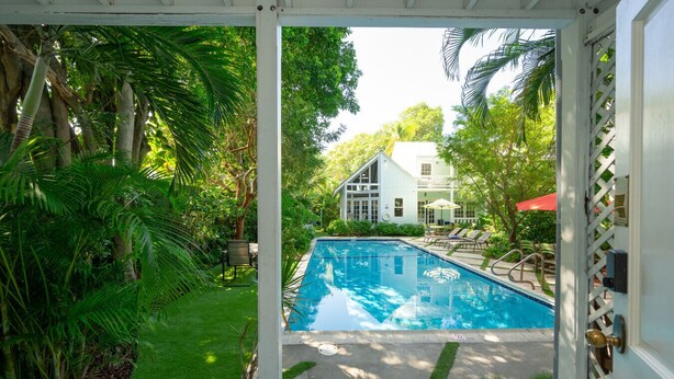 A pool area with a view of a house, surrounded by lush greenery.