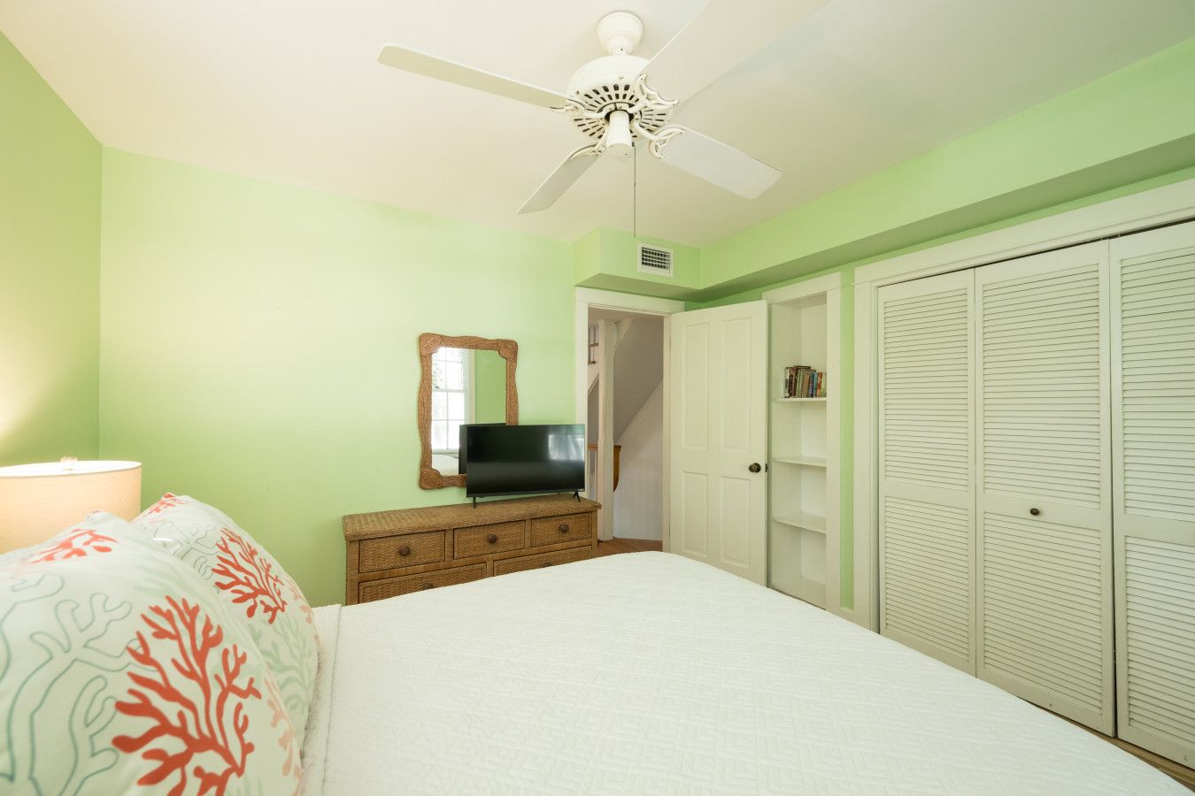 Une chambre à coucher avec un lit, un téléviseur posé sur une commode, un ventilateur de plafond et une armoire.