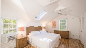 A bedroom with a large bed, two bedside tables, a ceiling fan, and a skylight.