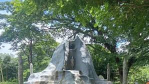 A rock formation with a statue at the top, surrounded by trees and a paved area. - Backpackers Temple  (Mae Sot)