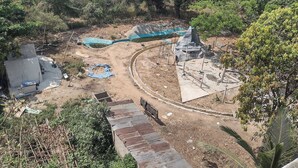 An aerial view of a construction site with a partially built structure, a blue water channel, and surrounding vegetation. - Backpackers Temple  (Mae Sot)