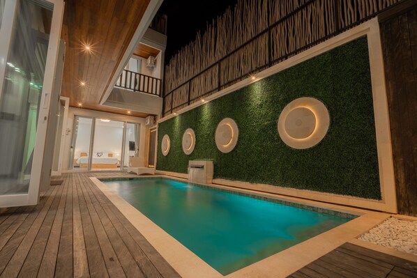 Ein Innenpool mit Holzboden, eine grüne Wand mit runden Leuchten und ein Balkon mit Geländer.