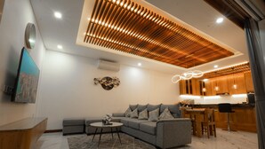 Una sala de estar moderna con un sofá modular, una mesa de centro redonda y una cocina con armarios de madera e iluminación colgante.