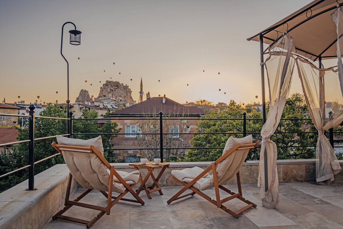 Una terraza con dos sillas de madera y una mesa, con vistas a un paisaje urbano que incluye edificios y una formación rocosa destacada.