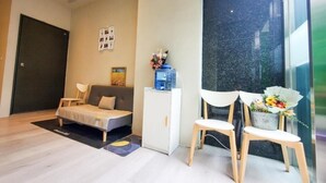 A modern living room with a sofa, a small table with a vase of flowers, a cabinet, and a large window. - Fashion home Hotel (Taipei)