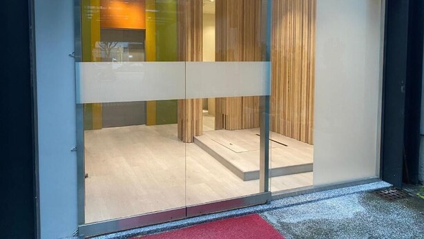 A modern hotel entrance with a glass door, wooden interior, and a red mat at the entrance. - Fashion home Hotel (Taipei)