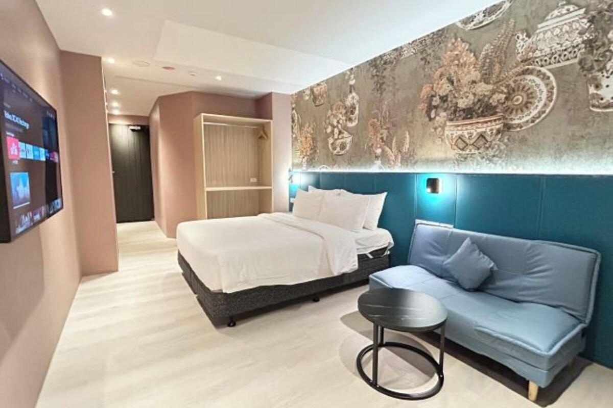 Una habitación de hotel moderna con una cama, un sofá, una mesita y un televisor montado en la pared.