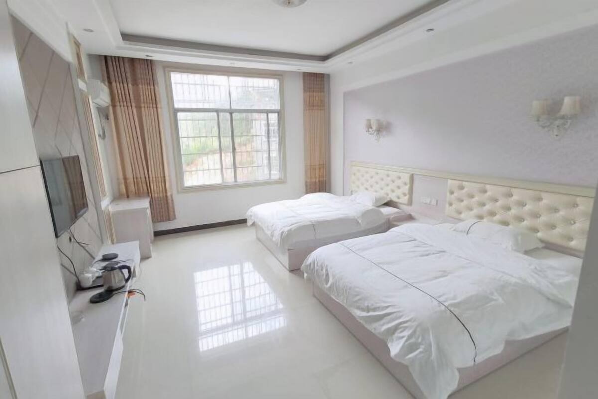 A hotel room with two beds, a TV, and a window with curtains.