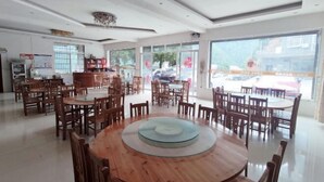Un comedor amplio con varias mesas y sillas de madera, ventanas grandes que dan a la calle y un techo con una lámpara decorativa.