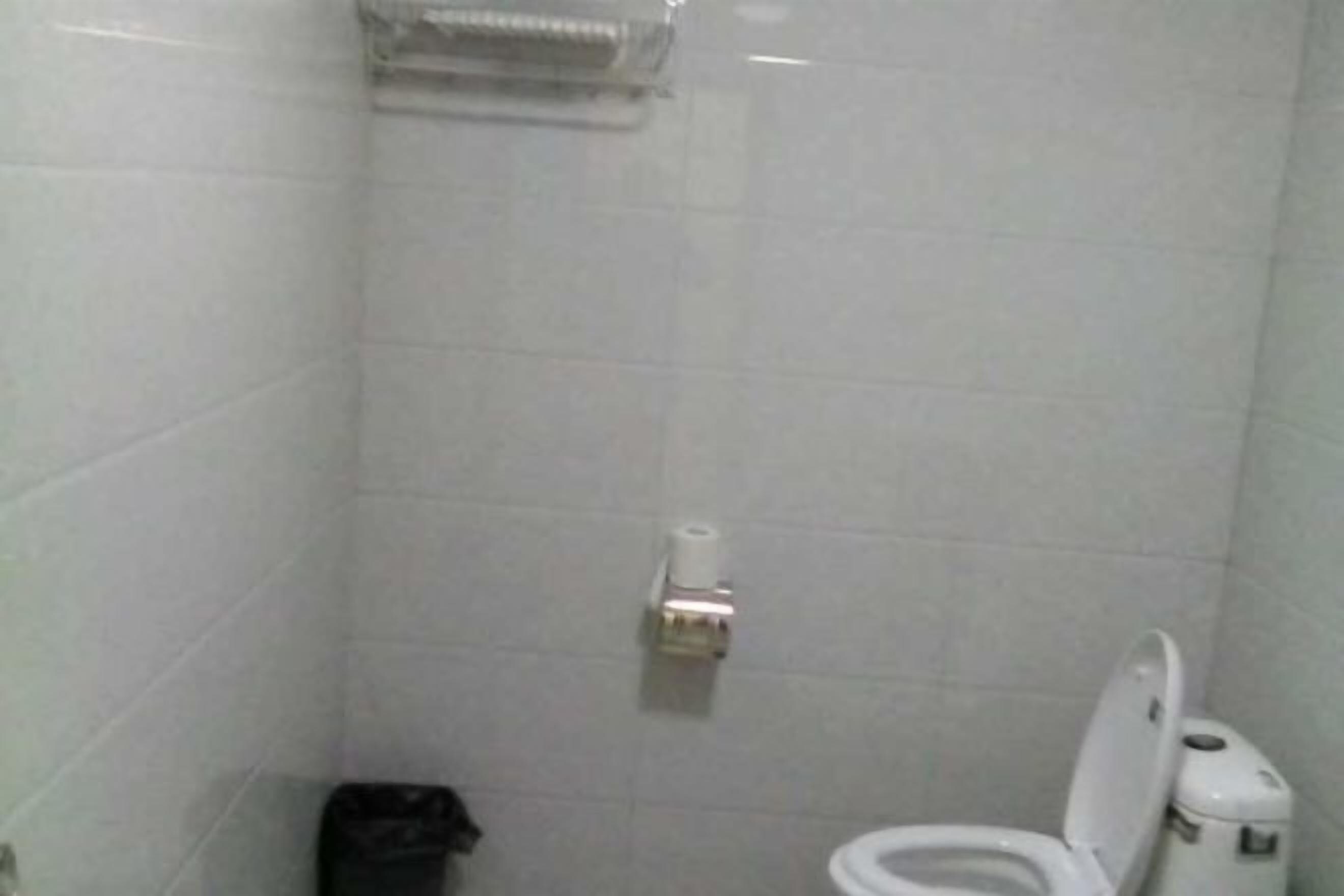 A small, tiled bathroom with a toilet, a trash bin, and a paper towel dispenser.