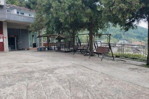 An outdoor area with a swing set, a covered seating area, and a building entrance. - Shuangpai Wuchenglou Hotel (Shuangpai)
