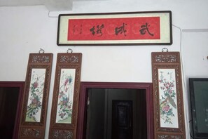Quarto tradicional chinês com uma placa vermelha, duas portas com motivos florais e uma obra de arte emoldurada acima.