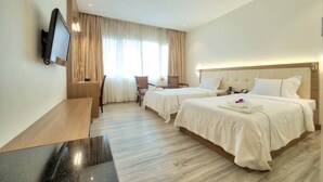 A hotel room with two beds, a desk, a chair, a TV mounted on the wall, and a large window with curtains. - Le President Hotel  (Phnom Penh)