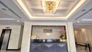 A hotel reception area with a modern design, featuring a reception desk, a chandelier, and a wall-mounted plaque. - Le President Hotel  (Phnom Penh)