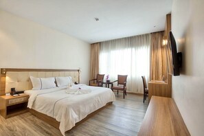 A hotel room with a large bed, a desk, two chairs, a TV, and a window with curtains. - Le President Hotel  (Phnom Penh)