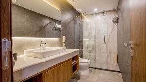 A modern bathroom with a large mirror, white sink, wooden cabinet, and a glass-enclosed shower area. - Le President Hotel  (Phnom Penh)