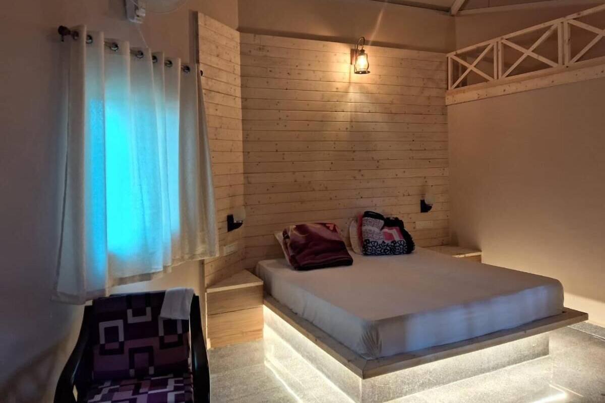 Quarto com cabeceira de madeira, cama com travesseiros, mesa de cabeceira e luminária fixada na parede.