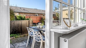 Blick auf eine Terrasse mit Tisch und Stühlen, einem Holzzaun und ein Haus im Hintergrund.