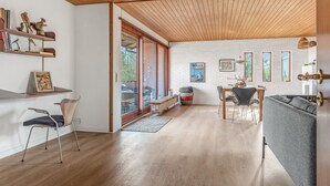 Amplia sala de estar con techo de madera, una mesa de comedor con sillas, un sofá y una estantería con objetos decorativos.