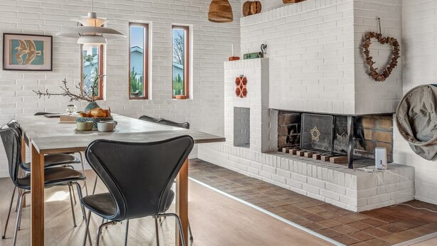 Un comedor moderno con chimenea de ladrillo blanco, techo de madera y vistas al exterior a través de ventanas.