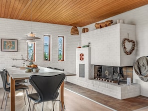 Un comedor moderno con chimenea de ladrillo blanco, techo de madera y vistas al exterior a través de ventanas.