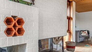 Una sala de estar moderna con una chimenea de ladrillo blanco, un sofá gris y un techo de madera.