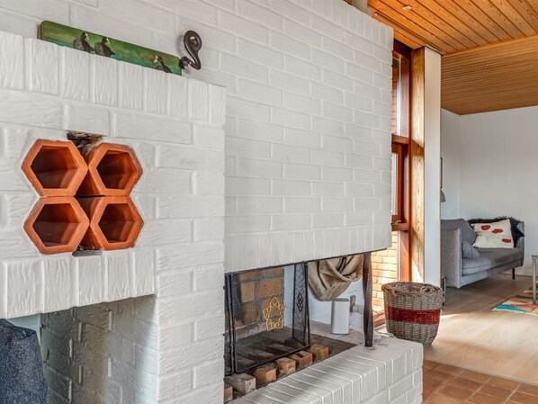 Una sala de estar moderna con una chimenea de ladrillo blanco, un sofá gris y un techo de madera.