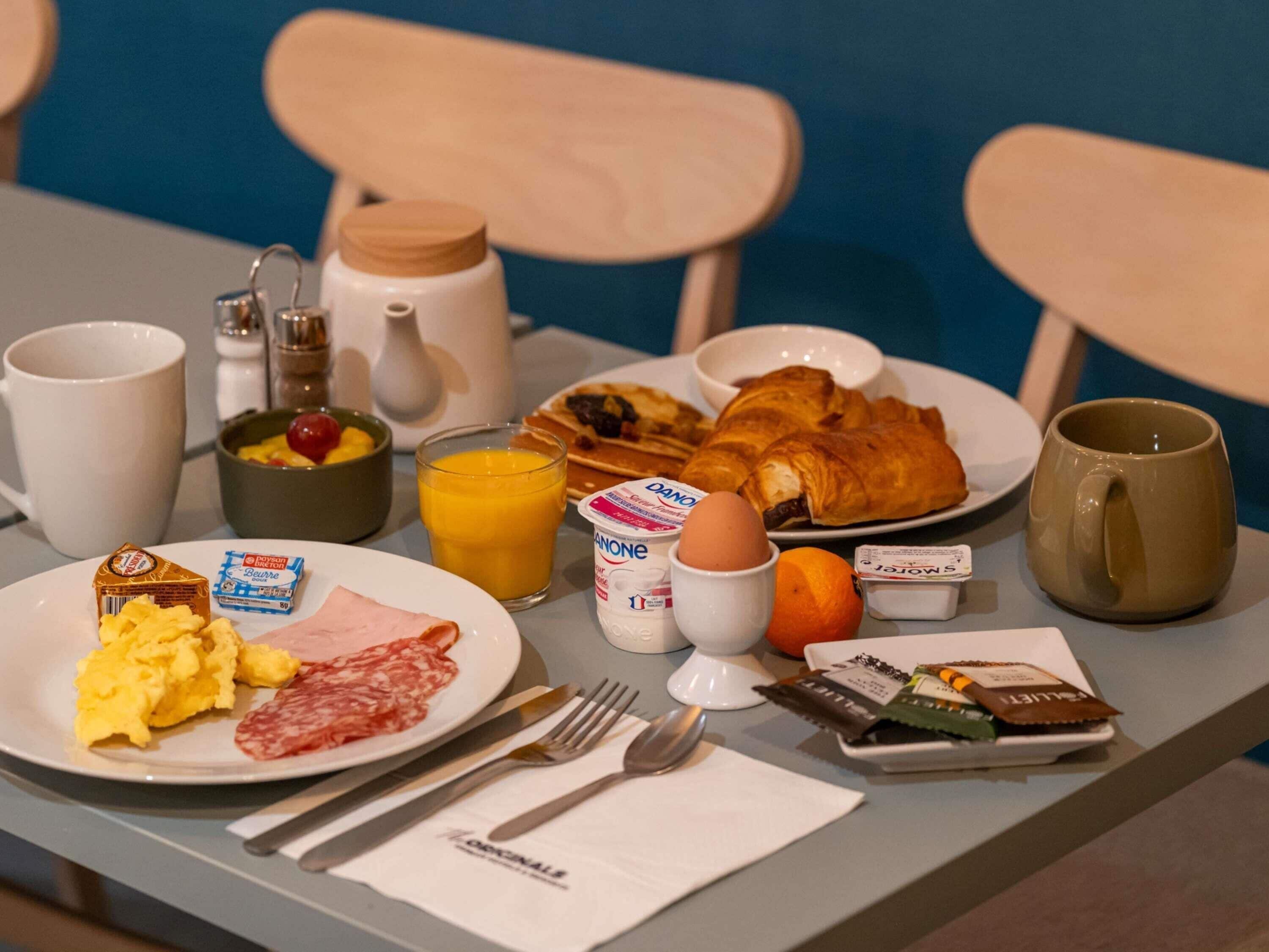 A breakfast table with plates of food, a glass of orange juice, a croissant, a coffee mug, and condiments.
