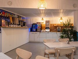 Zona de bar moderna con una máquina de café, estantes con botellas y un área de estar con mesas y sillas.