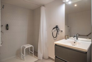 Un baño con ducha, lavamanos, espejo y toallero.