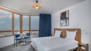 A hotel room with a large bed, a desk, two chairs, a view of the city, and a ceiling light. - Aparthotel Adagio Access Paris Sud Villejuif (Villejuif)