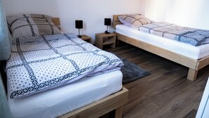 A bedroom with two beds, each with a wooden frame and a patterned bedspread. There are two bedside tables with lamps, and a gray rug on the floor.