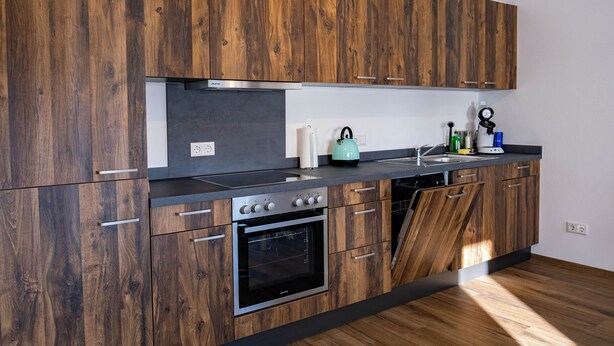 A modern kitchen with wooden cabinetry, a stainless steel oven, and a black countertop.